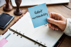 Woman holding a sticky note that says habit sustainability